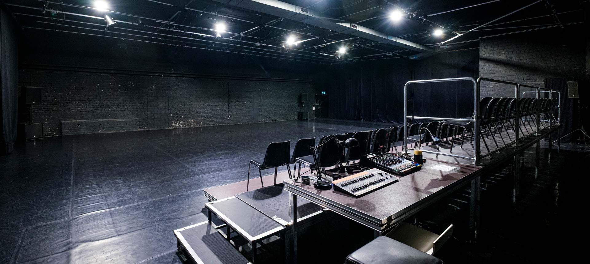Studio 1 / Black Box bei Barnes Crossing mit schwarzem Tanzboden, Zuschauertribüne, Stuhlreihen und Bühnentechnik. Blick aus dem Technikbereich über den Zuschauerraum auf die Bühne.
